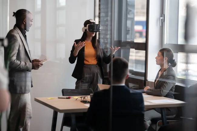 A woman with VR googles talking to a room of 3 people.