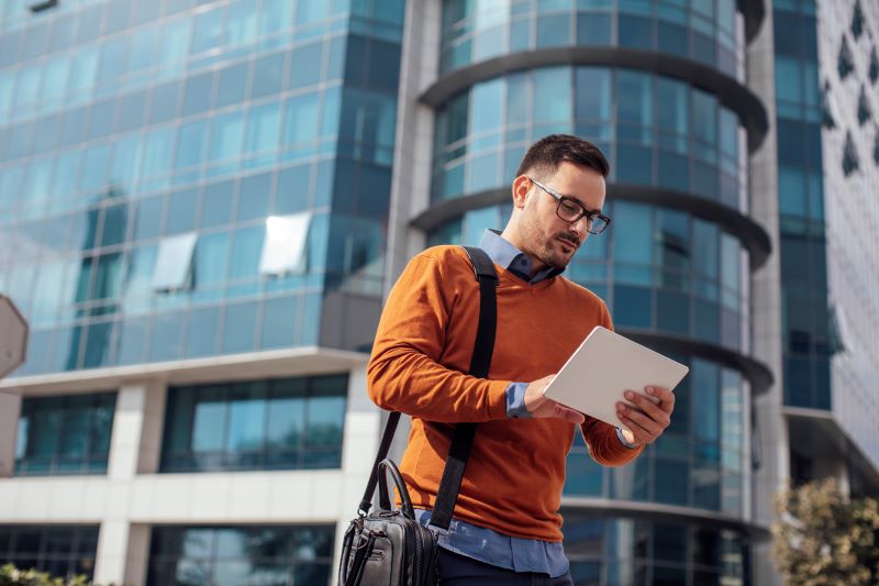 A man wearing an orange sweater is holding a tablet in his hands, looking focused on the screen.